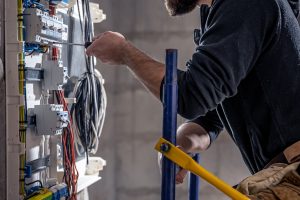 A male electrician works in a switchboard with an electrical connecting cable.